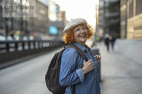 Happy senior woman with backpack on footpath