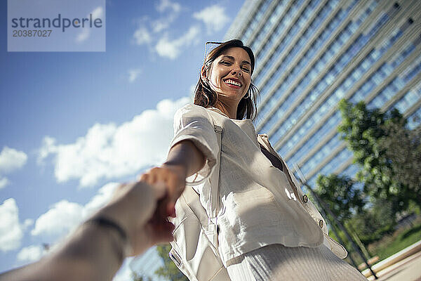 Happy young woman holding hand of man on street