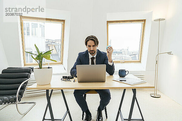 Businessman with globe using laptop sitting at desk in office