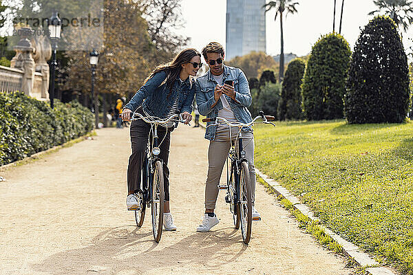 Man sharing smart phone with girlfriend on bicycle at park