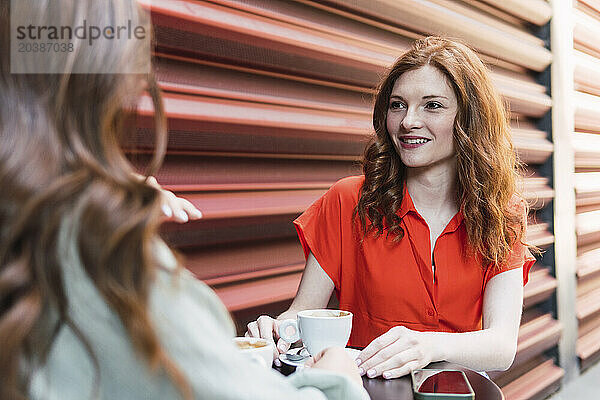 Smiling woman talking with friend near shutter at sidewalk cafe