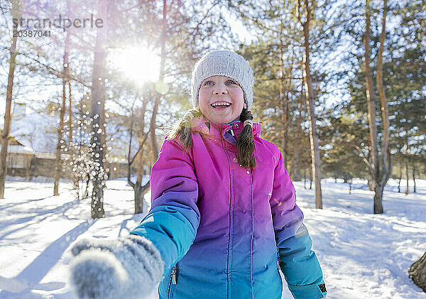 Happy girl playing with snow in winter forest on sunny day