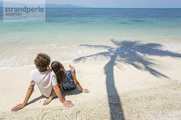 Couple looking at sea sitting on sand at beach