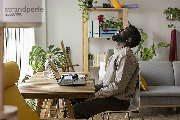 Tired freelancer sitting with eyes closed and laptop at desk