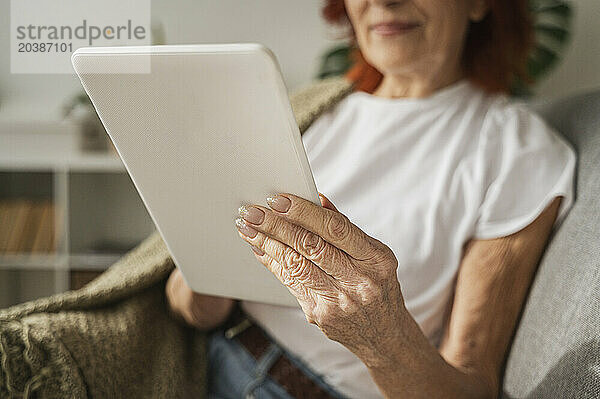 Retired woman with digital tablet sitting on sofa at home