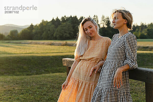 Thoughtful friends leaning on wooden railing in park