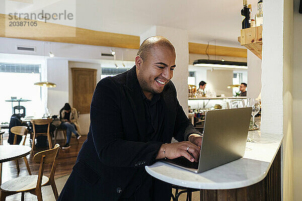 Smiling customer using laptop sitting at illuminated table in restaurant