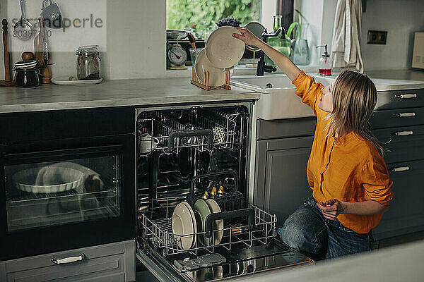 Woman stacking washed plates on kitchen counter at home