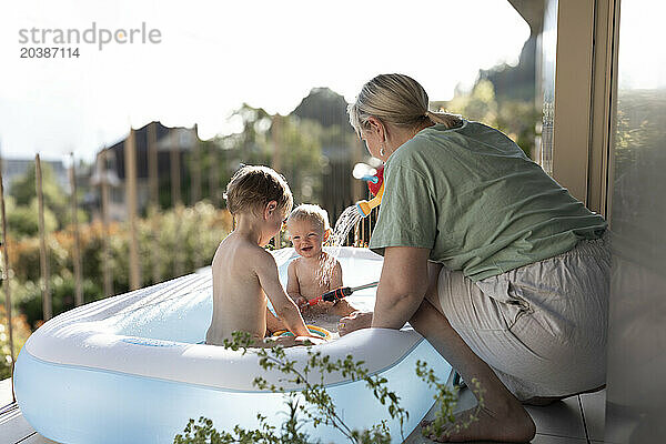 Mother bathing children in inflatable tub at balcony