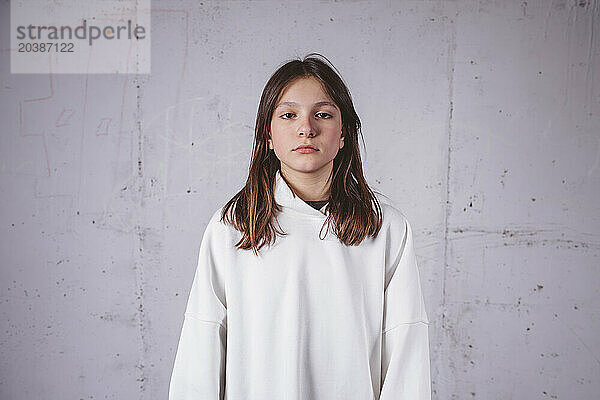 Serious girl in white hoodie in front of gray cement background