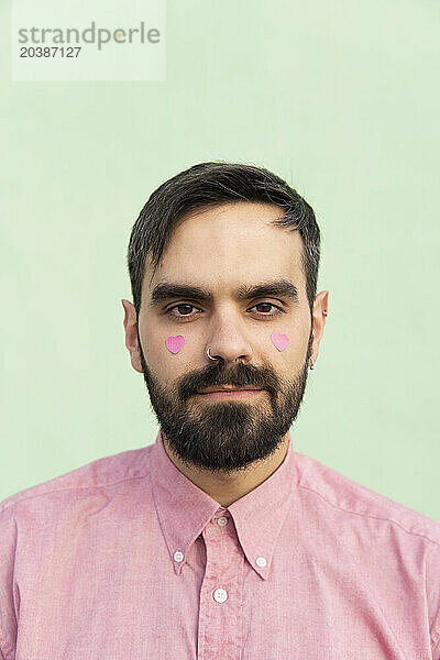 Man with pink heart shape stickers on cheeks against mint green background