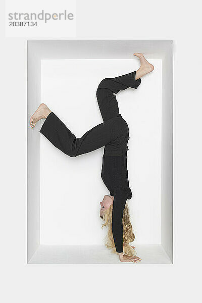 Teenager doing handstand in alcove against white background