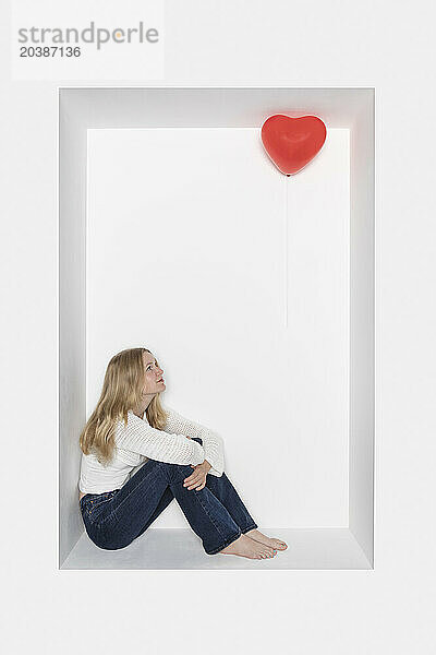 Teenage girl sitting on alcove by heart shape balloon