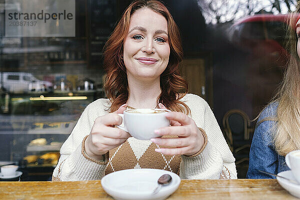 Smiling woman holding coffee cup and sitting in cafe