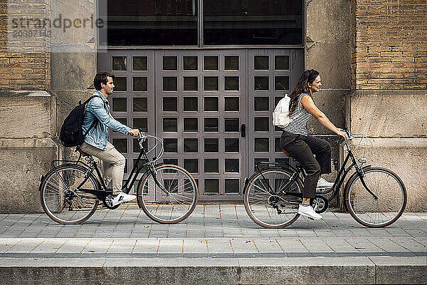 Couple cycling near building on sidewalk