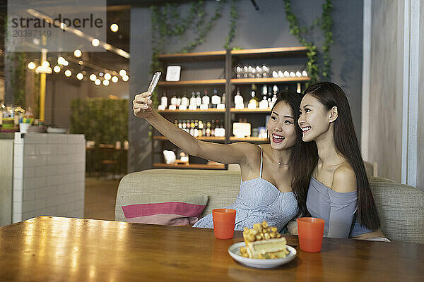 Smiling friends taking selfie through smart phone at restaurant