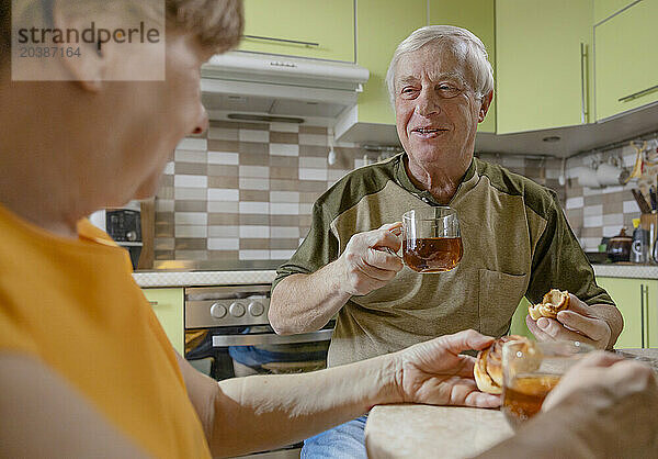 Smiling man having sweet buns and tea together with woman at table