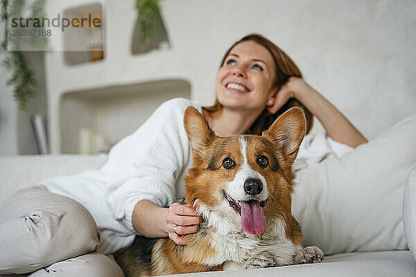 Happy woman sitting with dog on couch at home