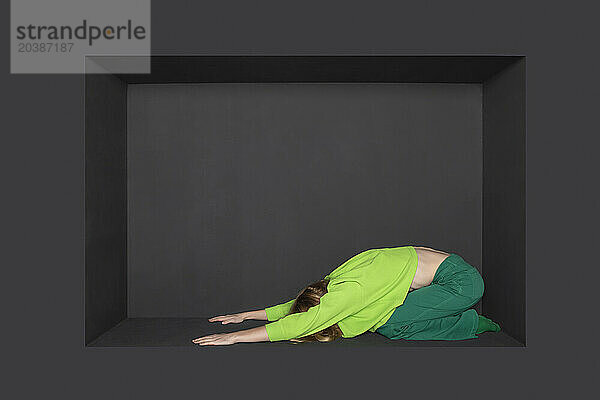 Teenage girl practicing yoga in alcove against black background