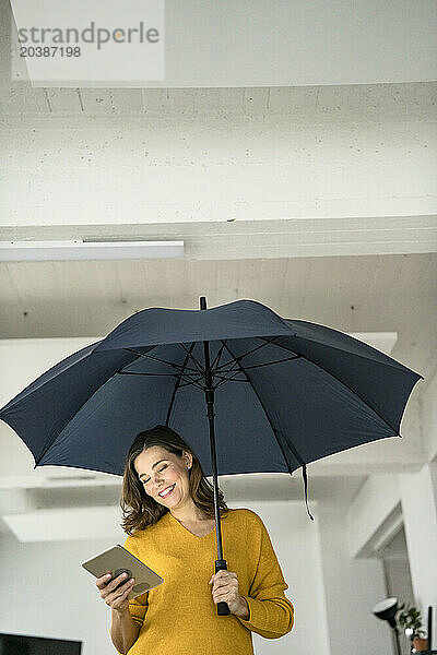 Smiling creative businesswoman with tablet PC holding open umbrella in office