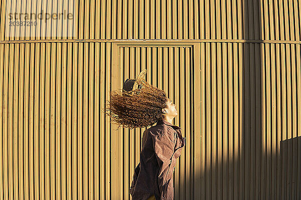 Young woman with windswept hair in front of orange metal wall