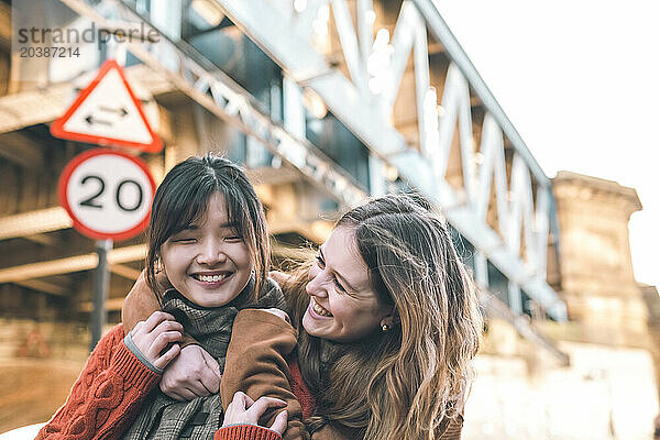 Cheerful woman embracing sister near bridge