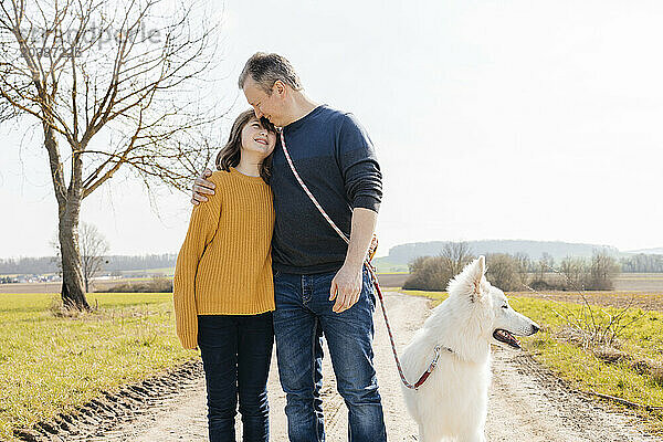 Father and daughter standing with white Swiss Shepherd on footpath