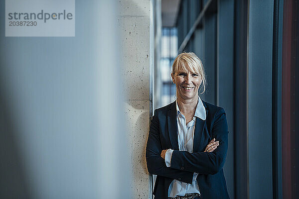 Smiling businesswoman standing with arms crossed in corridor