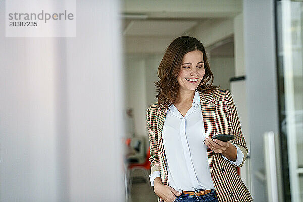 Smiling businesswoman holding mobile phone in creative office