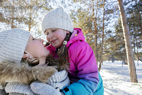 Smiling girl embracing mother in winter forest