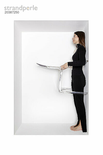 Girl with chair standing in alcove by white background