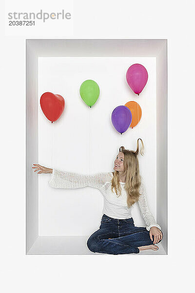 Teenage girl with multi colored balloons sitting in alcove