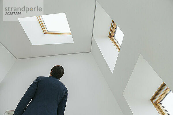 Businessman standing at white office with windows and skylight