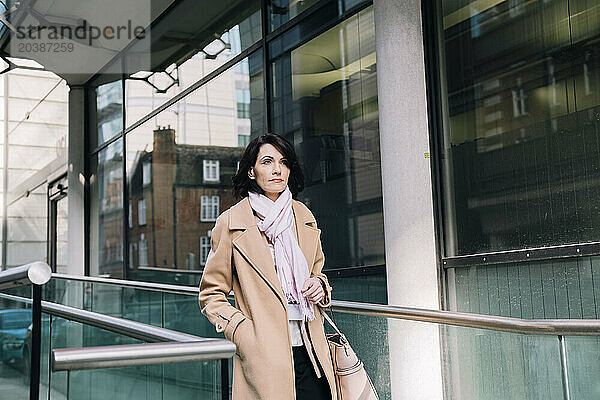 Confident mature businesswoman wearing overcoat walking with hand in pocket