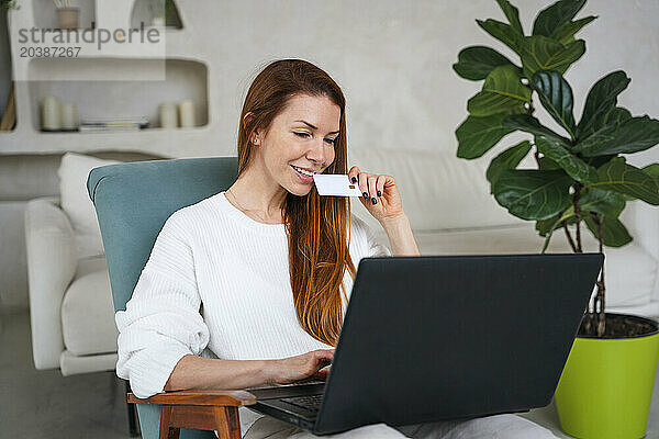 Smiling woman with credit card shopping online through laptop at home