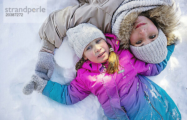 Mother and daughter lying on snow in winter