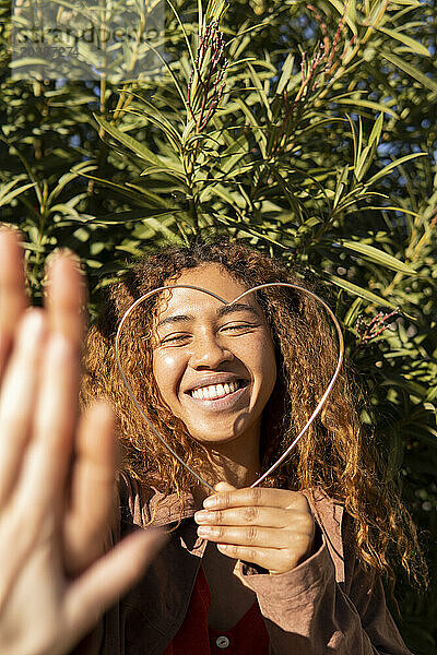 Happy young woman holding metal heart shape giving high-five to friend on sunny day