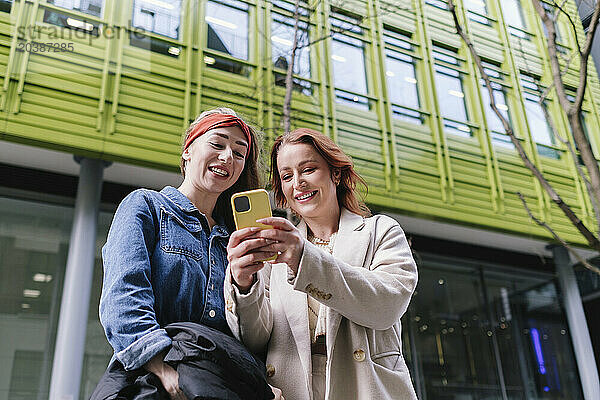 Happy friends using smart phone in front of building