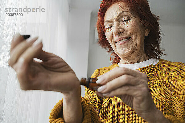 Smiling senior woman applying essential oil on wrist at home