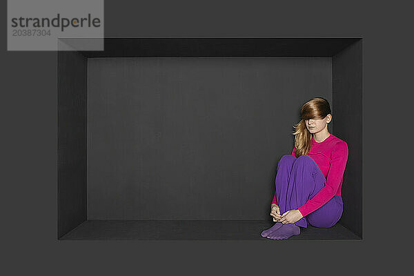 Blond teenager sitting in alcove against black background