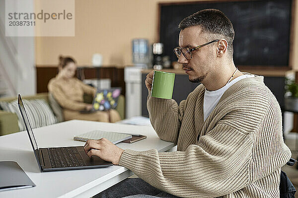 Businessman having tea and working on laptop at office