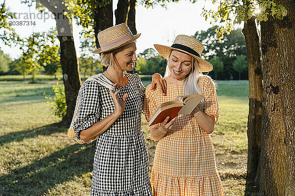 Smiling woman sharing book with friend standing in park