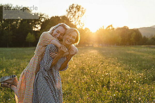 Smiling woman carrying friend on piggyback in park