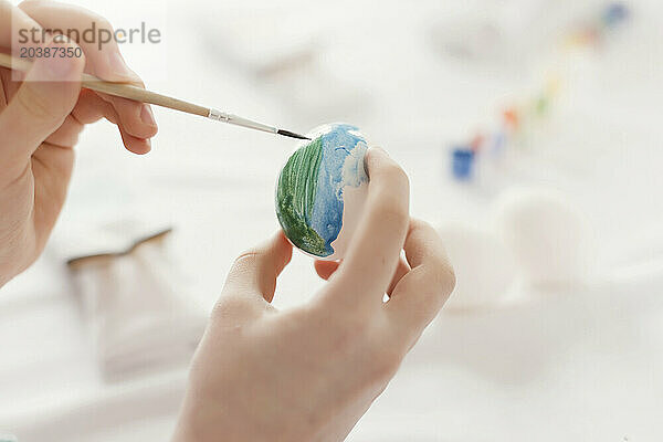 Hands of girl painting Easter egg using brush at home