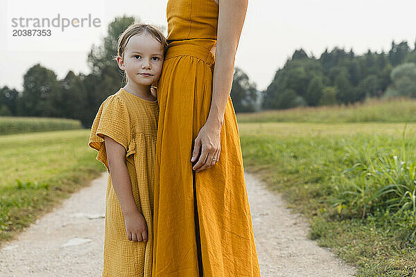 Girl standing with mother on footpath in meadow