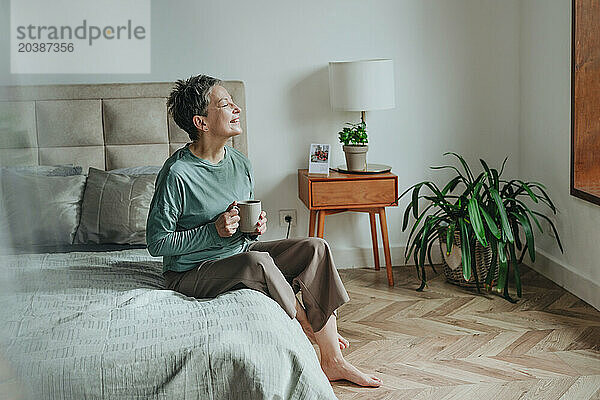 Smiling woman enjoying coffee sitting on bed at home
