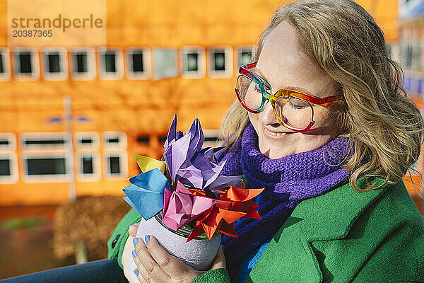 Smiling woman holding colorful origami flowers at sunny day