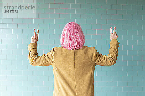 Woman gesturing peace sign near turquoise wall