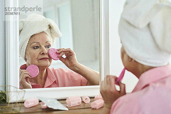 Woman wearing towel and taking care of skin looking in mirror at home