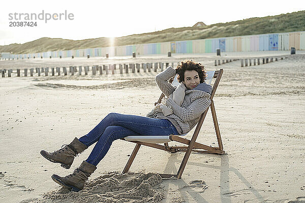 Smiling woman sitting on deck chair relaxing at beach